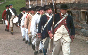 Soldiers march in file. All wear woolen jackets or white linen shirts, and large black hats. Everyone carries a musket. Soldiers march in file. All wear woolen jackets or white linen shirts, and large black hats. Everyone carries a musket.