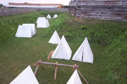 a grassy green area with white tents dot the edges of the forts walls