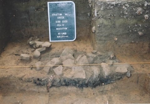 Several large, irregularly shaped rocks with a burn layer below the rocks. Image is a profile picture of the hearth.