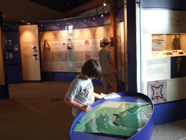 A young man stares at a blue and green map, the sun reflects off of the shiny textured surface as he traces it