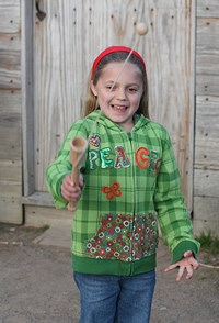 a little girl with a bright smile & green shirt plays on a brown parade ground with a cup, string, and ball toy. a little girl with a bright smile & green shirt plays on a brown parade ground with a cup, string, and ball toy.