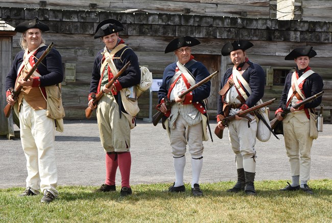 A photo of 4 people dressed as Continental soldiers. They stand in formation with their muskets moving in unison.