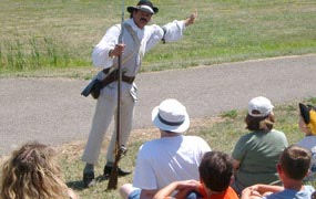 a tall man stands, highlighted by bright sun on a path. he points in the distance, a crowd follows his gestures a tall man stands, highlighted by bright sun on a path. he points in the distance, a crowd follows his gestures