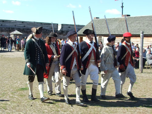 several men in blue & red uniforms march in-step holding their weapons at their shoulder.