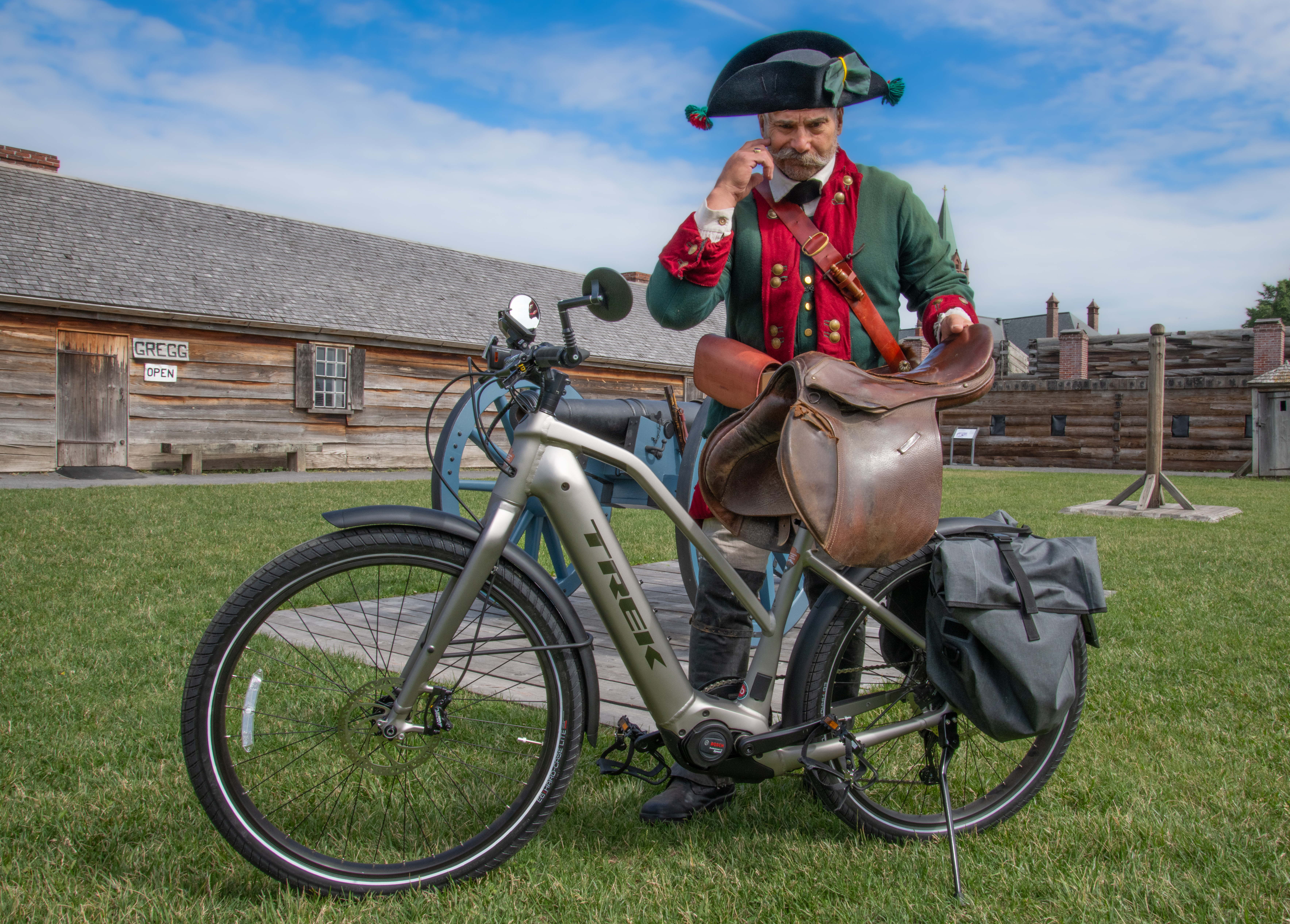 Biker.Cred.NPS.RangerDanU.D85_5964 A man with a handlebar mustache and an 18th Century soldier's uniform stands at the side of a bicycle, considering how it works.