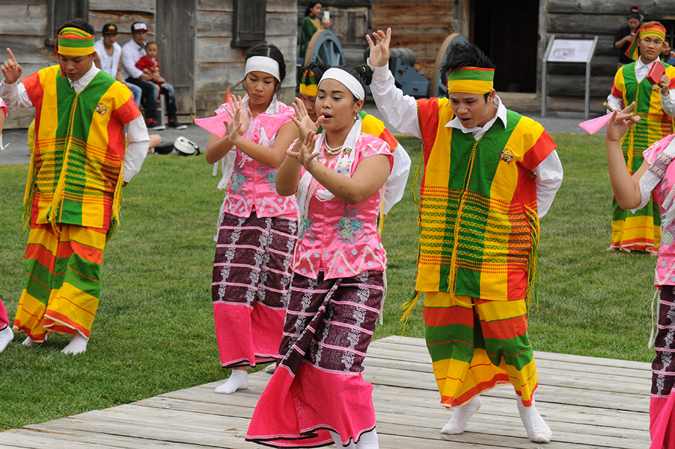 Men and women in colorful striped garb dance together in front of a crowd.