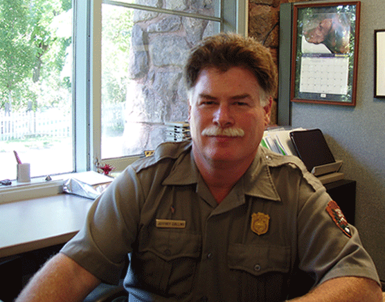 a man with bright red hair and mustache sits in front of a window and smiles