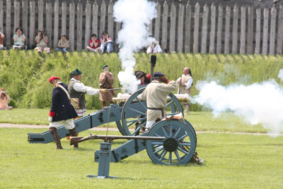 white smoke billowing from a blue cannon carriage-a crew of 6 men huddle round and get to work