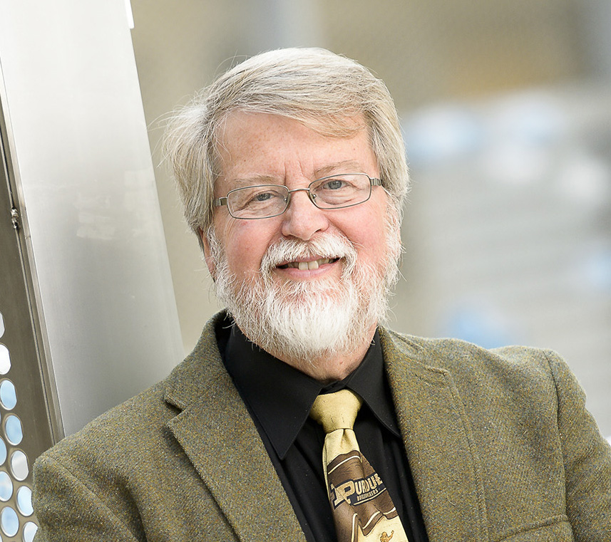 A close up of an older man with a beard wearing glasses, a goatee, a suit, and tie.