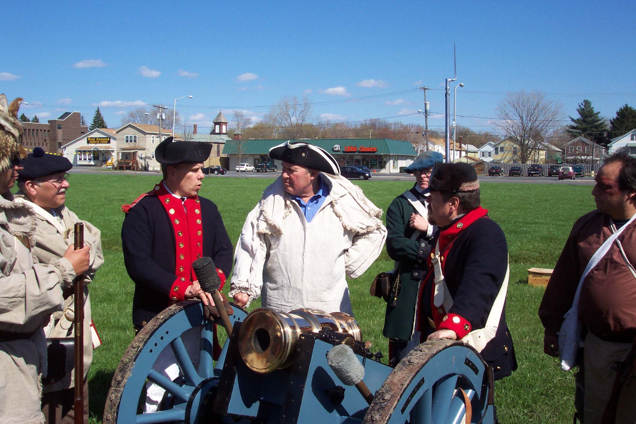 several men stand near a small cannon in 18th century clothing.