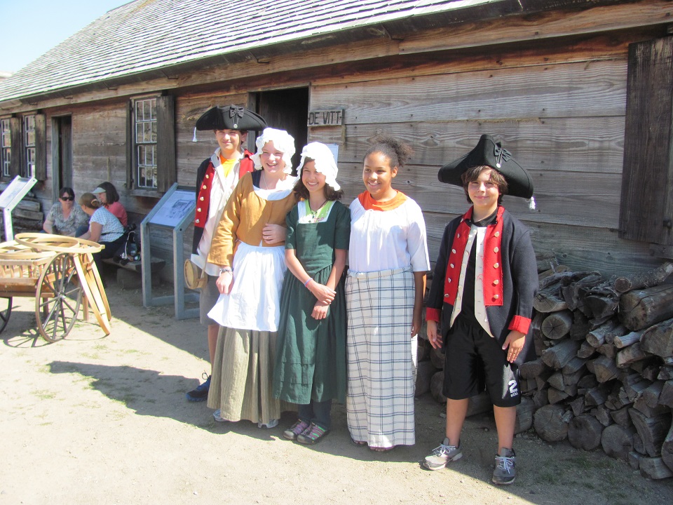 Four children stand smiling while showing off colorful old-fashioned clothing.