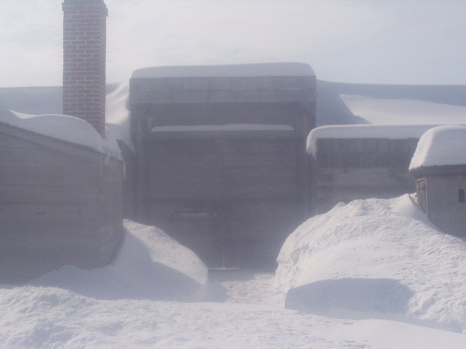 Fort Stanwix in winter, a white wall with a small brown gate pops through the snow.