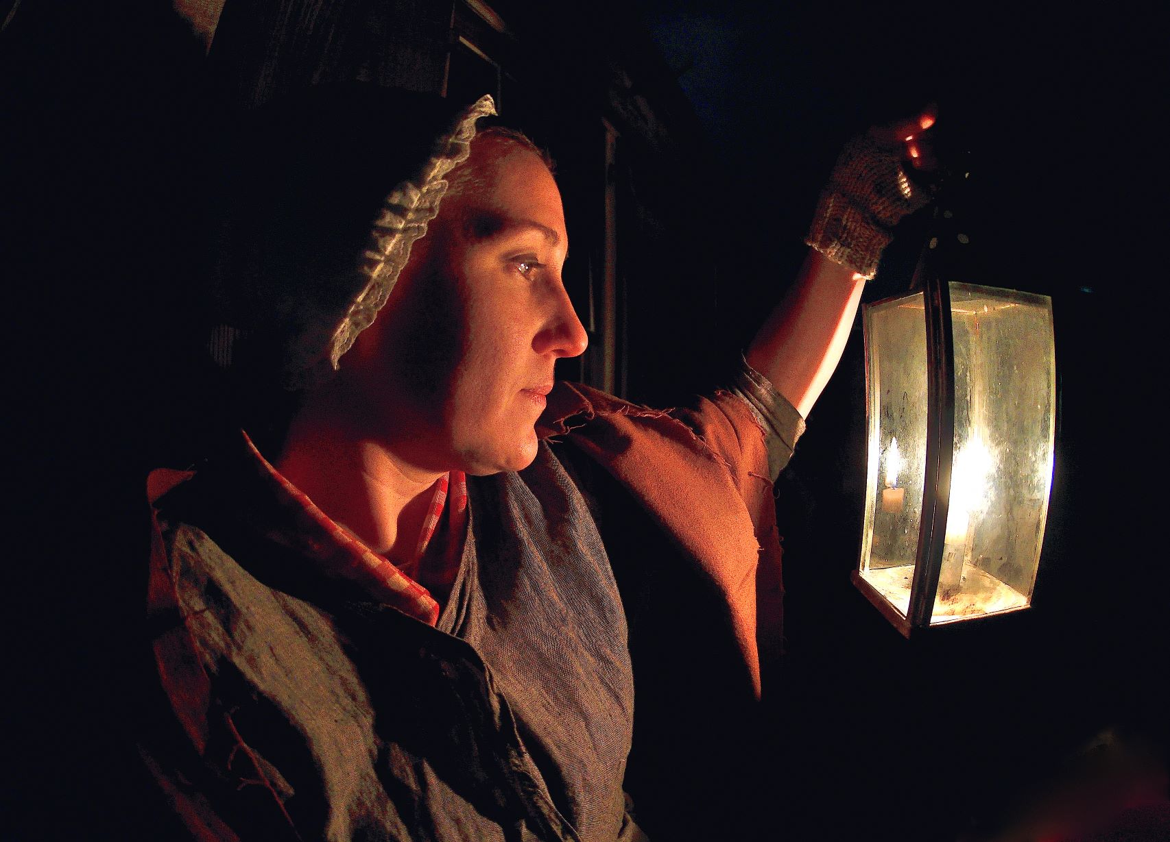 A woman stands in the dark, her face illuminated by soft candlelight.
