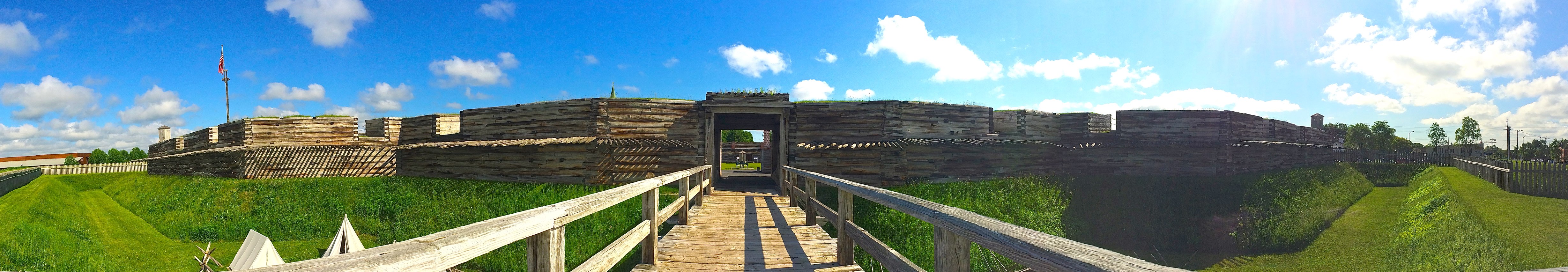 In front of you, a log cabin-style building stretches in front of you. You see a wooden bridge over a grassy ditch.
