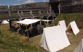 a verdant green ditch, white tents, under which people move back and forth, climbing in and out, doing daily activities