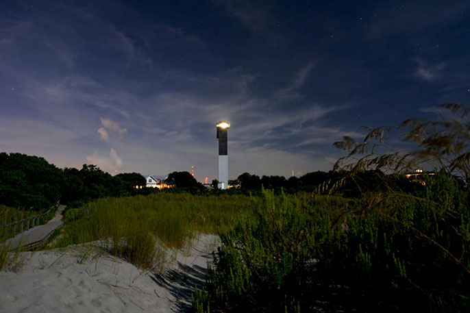 The Sullivan's Island Lighthouse with its light shining as viewed from the beach