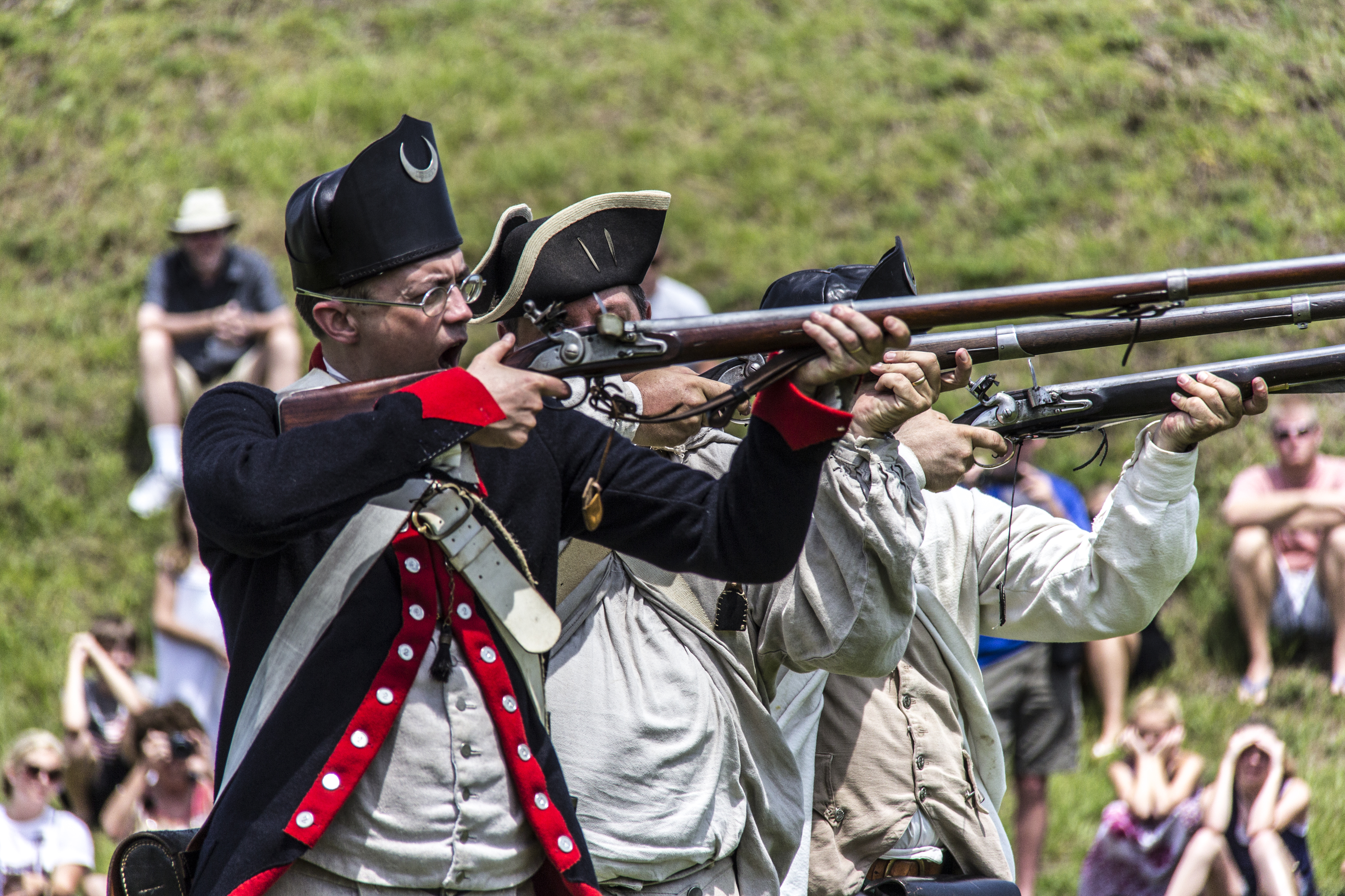 Reenactors firing muskets in uniform representing soldiers from the American Revolution