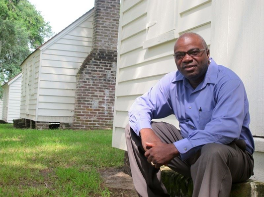 Joe McGill of the Slave Dwelling Project sitting in front of a historic cabin. Joe McGill of the Slave Dwelling Project sitting in front of a historic cabin.