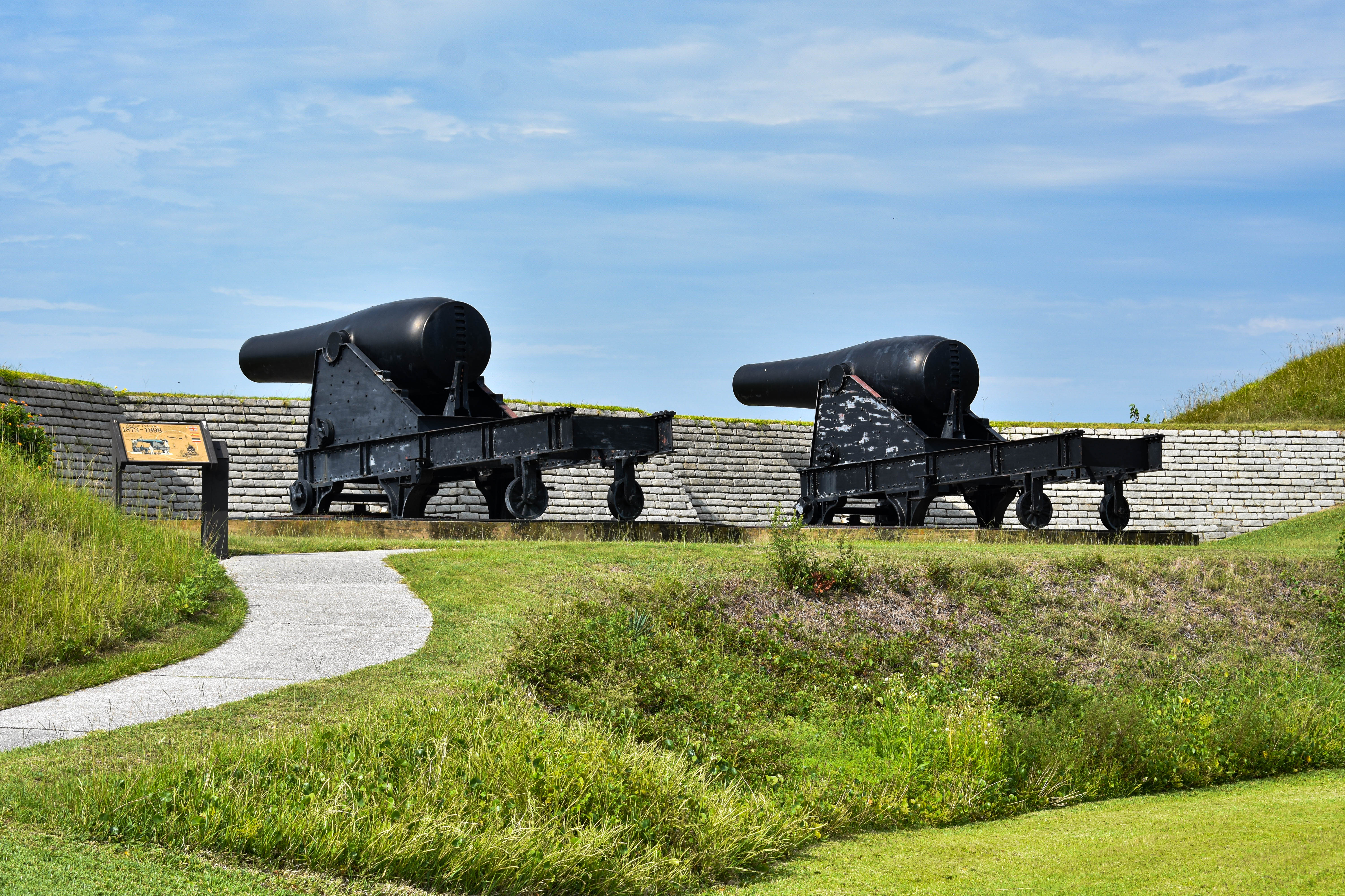 Two large black cannons face to the left, over Fort Moultrie's walls on a clear day. No clouds in the sky.