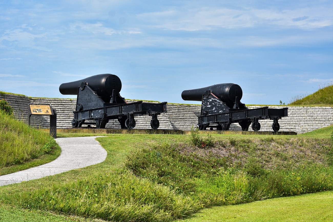 Two large black cannons face to the left, over Fort Moultrie's walls on a clear day. No clouds in the sky.