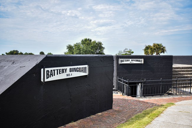 A black battery facing into Charleston Harbor at Fort Moultrie. There is a red brick path in front of it.