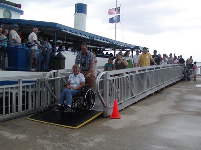 A visitor in a wheelchair descends the ramp from the boat to the Fort Sumter dock.