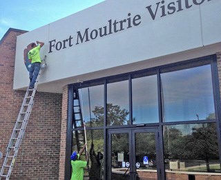 Contractor standing on ladder repainting entrance to Fort Moultrie Visitor Center