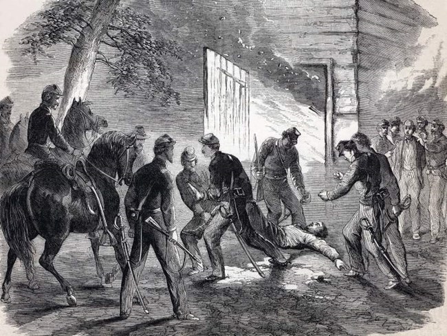 Woodcut engraving of Booth being dragged out of a burning barn by six cavalry soldiers as other soldiers stand nearby holding another man (Herold) captive