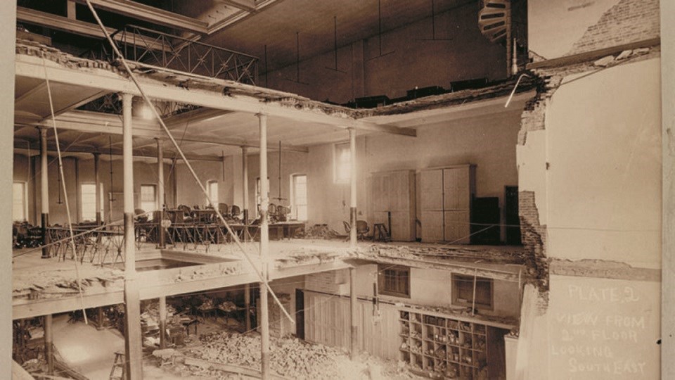 black and white photo showing three story building where the floors have partially collapsed about half way. The ground floor is covered with rubble.