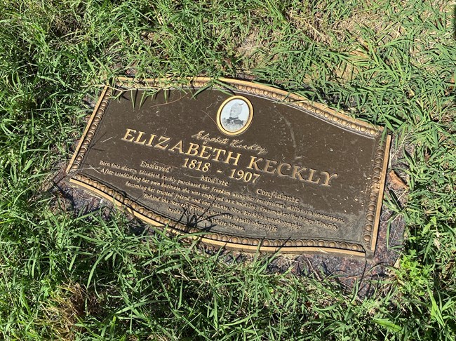 Surrounded by grass, bronze plaque grave marker with Elizabeth Keckly's name and biographical info, with an of an older Elizabeth in an oval frame at the top.
