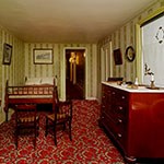 color photo of bed, chairs and bureau. red carpet