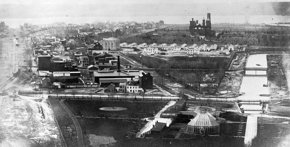 Black and white photo showing an expansive view of the National Mall in 1863, with many buildings, open spaces, and a canal running through the center.