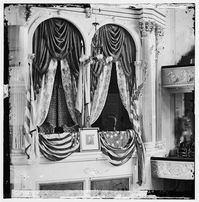 Box seats above the stage decorated with Flags and a portrait of Washington