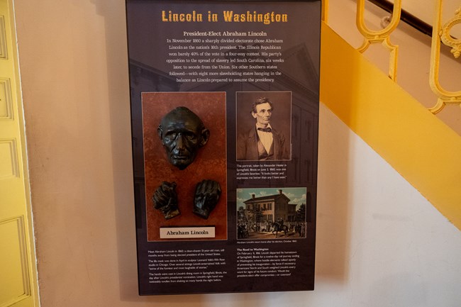 An exhibit panel mounted on a wall with text, photos, and a bronze cast of a man's face and hands.