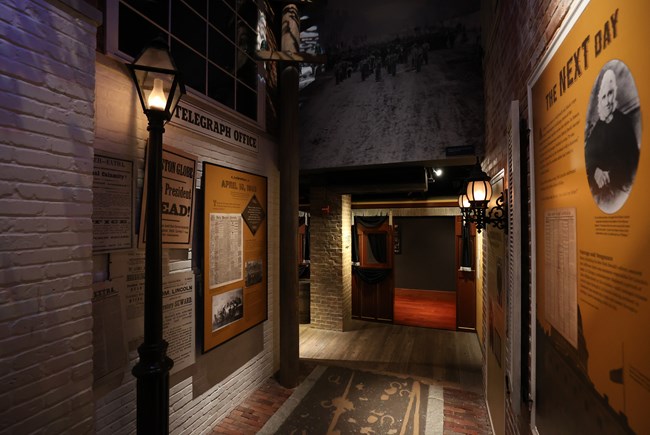 A hallway imitating an alleyway with a streetlight, brick walls, and exhibit panels with photos and text.