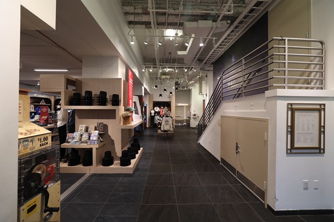 A carpeted room with displays of hats and t-shirts on the left and a staircase with railing on the right.