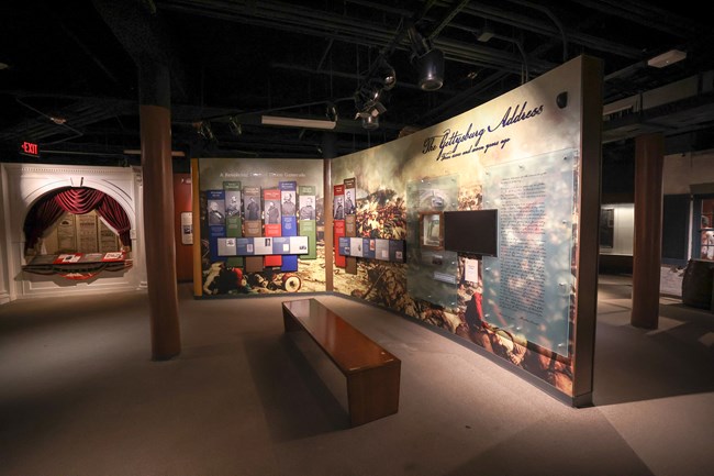 A dimly lit room with a bench in front of a video screen and informational panels on the wall with photos and text.