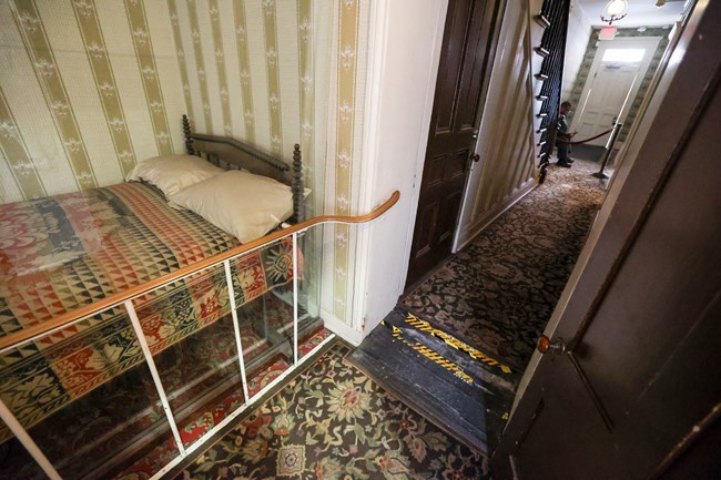 A bed behind a railing next to a doorway with a ramp into a narrow hallway.