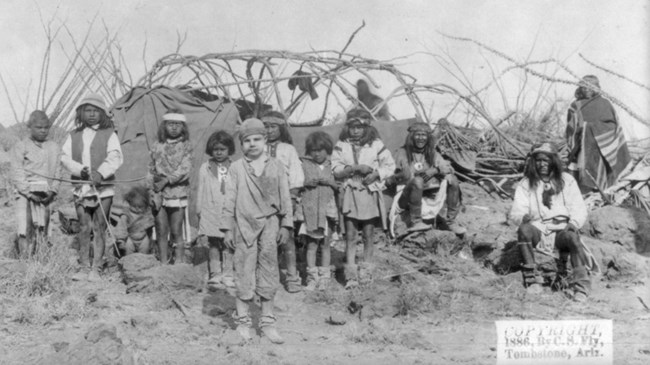 young white boy wearing skullcap standing amid Apache children