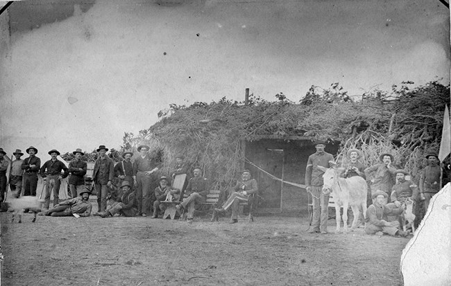 group of soldiers standing in front of earthen fort decorated with branches