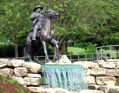 statue of buffalo soldier riding horse at edge of small waterfall