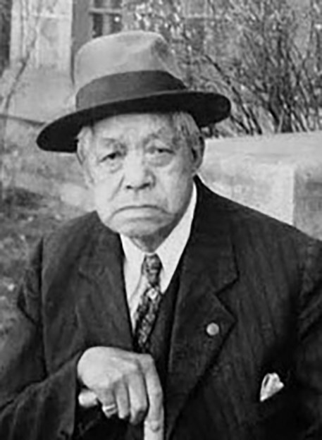 older asian gentleman  wearing hat and suit jacket, resting his hand on a cane