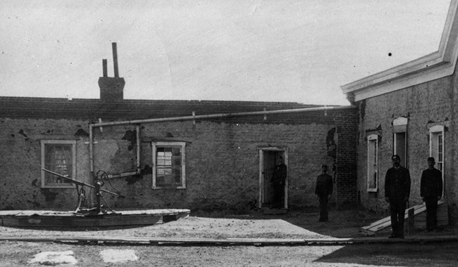 19th-century army medical personnel standing in front of building with gutters draining into cistern