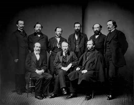 Image of Army officers in dark civilian clothing, with six men standing in a rear row and three men seated in front of them