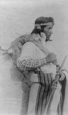 male pueblo indian holding rifle and a dead animal slung over his shoulder