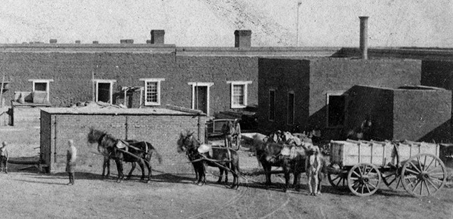 mules hitched to a heavily loaded wagon standing in front of two brick structures