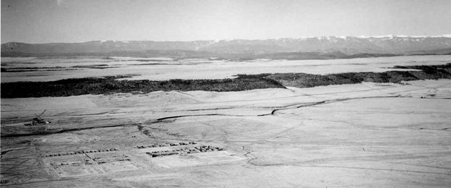 Black and white aerial photograph showing ruins of fort union with Black Mesa beyond and Rocky Mountains in the background.