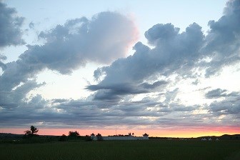 White walled structure in a grassy field at sunset beneath a cloudy sky.