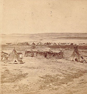 Small log structure with tipis around it in a field.