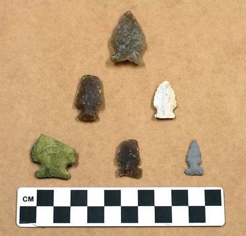 Six rough cut sharp tipped stone triangles. There are three brown ones, one white one, one gray one, and one green one.